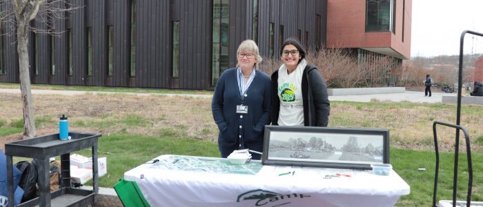 UConn tree warden and student from Office of Sustainability pose behind Earth Day table for Class tree Planting